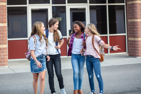 Four girls with backpacks talking to one each other in front of a school