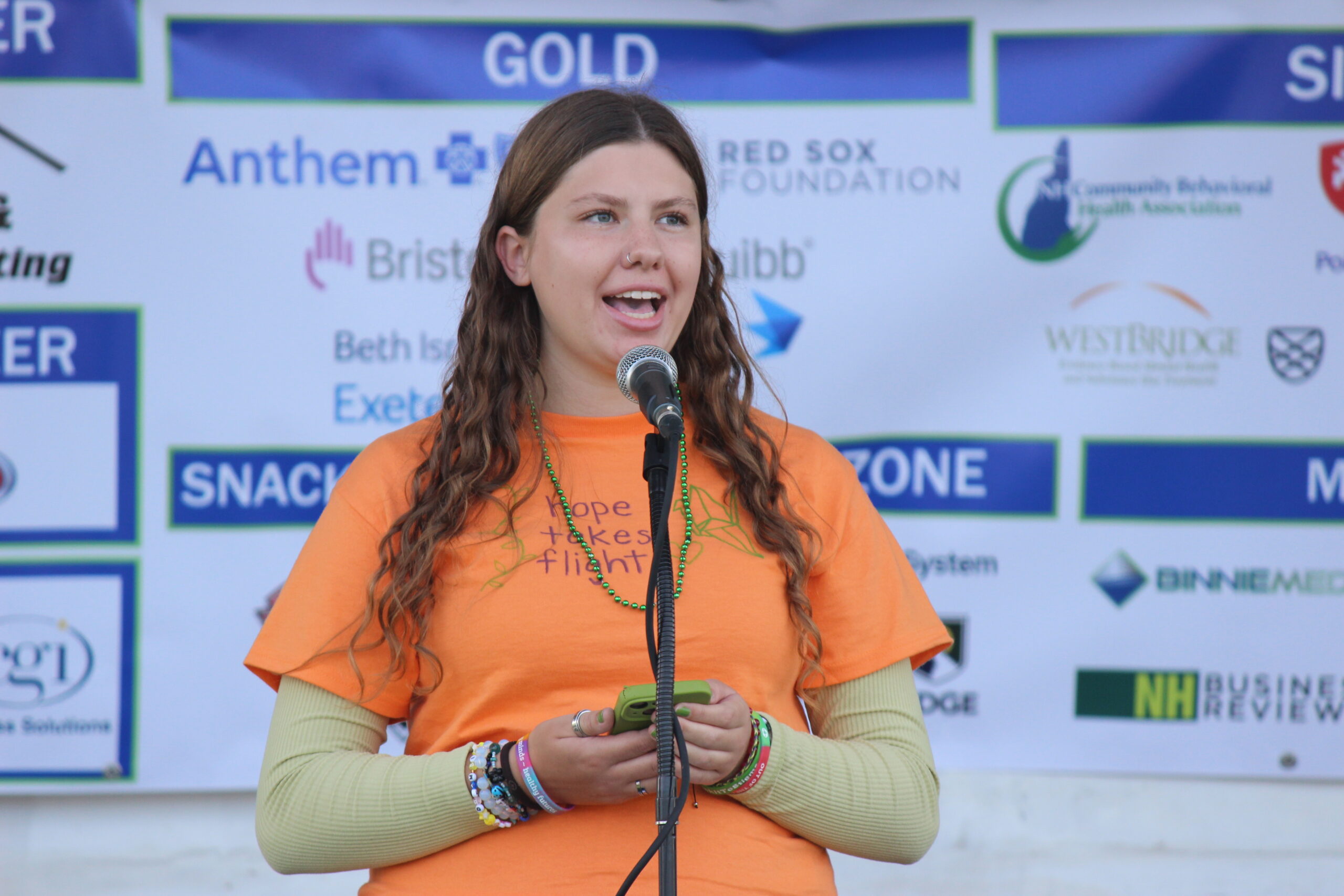 Young girl with an orange shirt speaking into a microphone